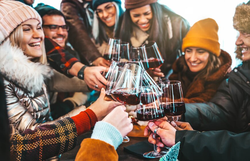 Friends clinking red wine glasses together wearing winter clothes