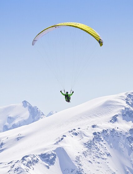 Paraglider with yellow wing above snowy peaks