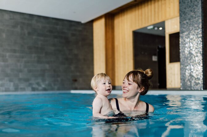 Smiling young woman holding toddler in Bear Lodge swimming pool