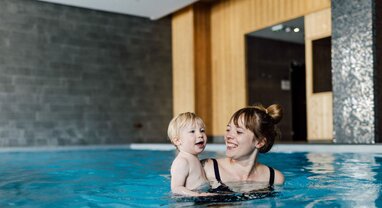 Smiling young woman holding toddler in Bear Lodge swimming pool