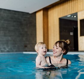 Smiling young woman holding toddler in Bear Lodge swimming pool