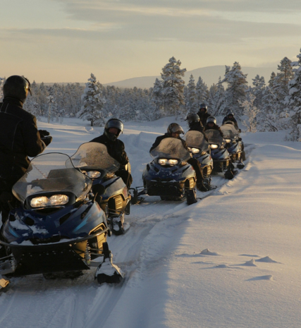 Group of people on skidoos behind guide in snowy evening setting