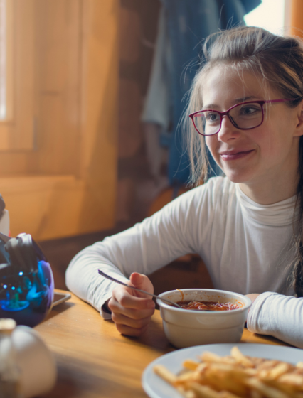 Smiling young girl eating lunch at mountain ski restaurant with ski helmet on table