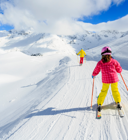 Young girl skiing behind mother on trail between pistes