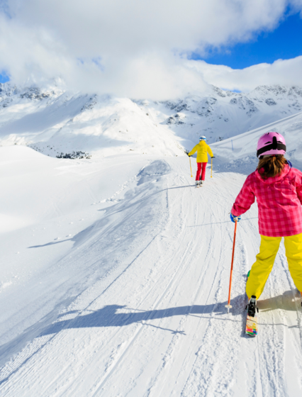 Girl in bright ski clothing skiing behind parent