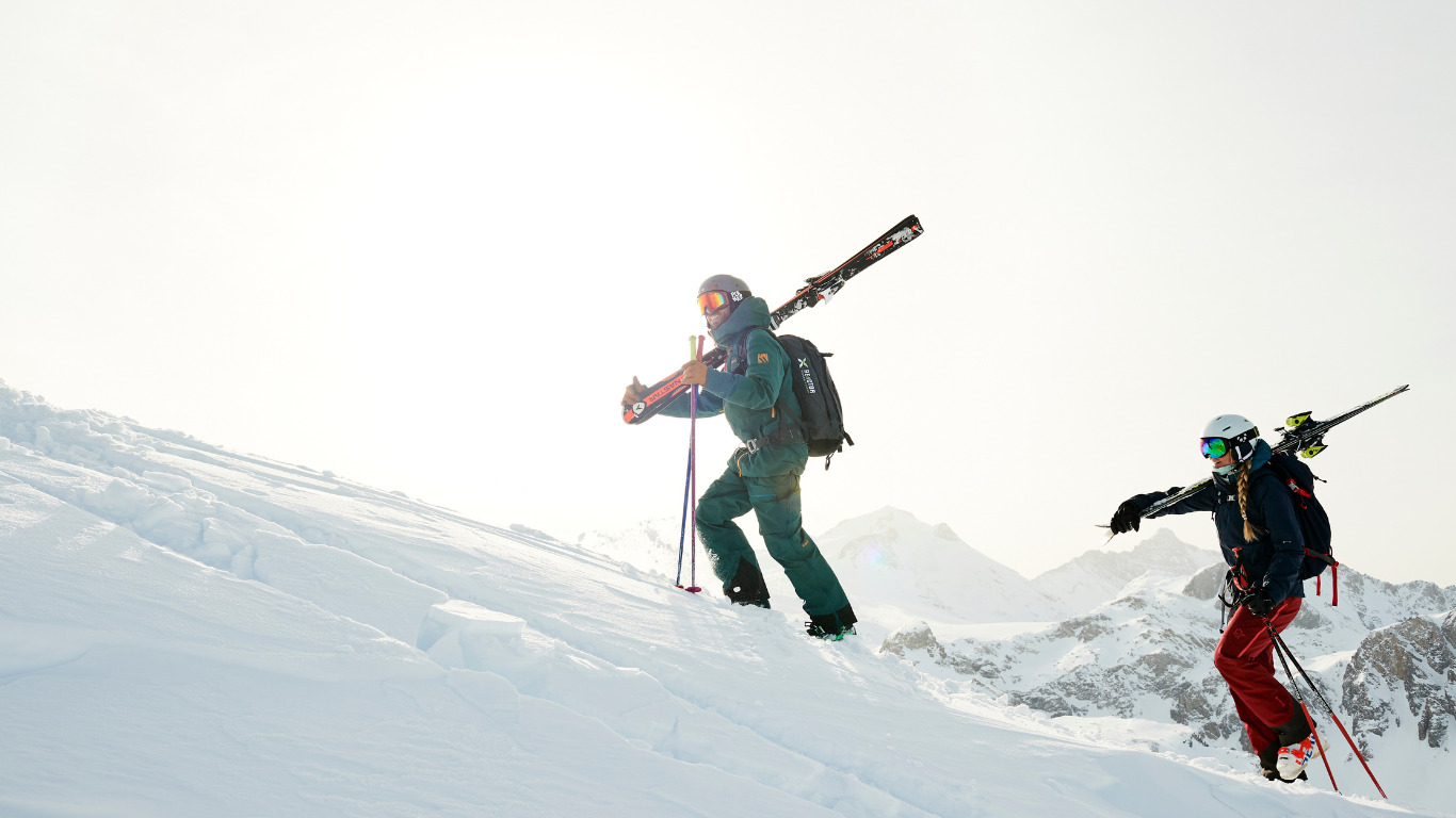 Female skier and male TDC ski instructor hiking up snowy slope with skis on shoulders