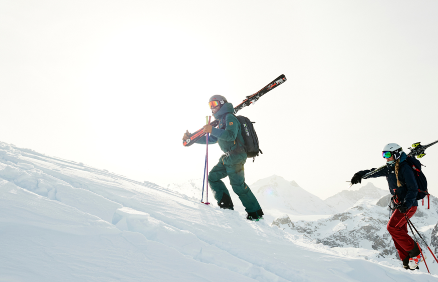 Female skier and male TDC ski instructor hiking up snowy slope with skis on shoulders