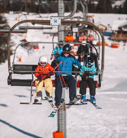 Smiling adult skier with two young children either side of them on chairlift in Morzine