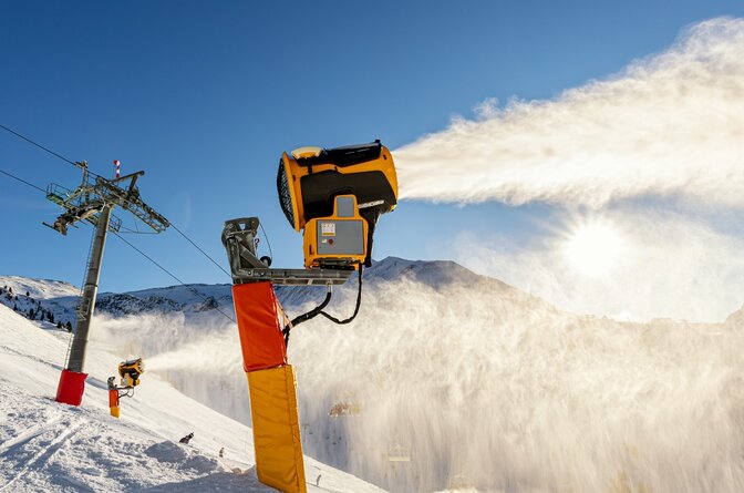 Snow cannons producing snow on ski runs on sunny day