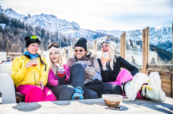 Four friends in ski clothing sitting on mountain restaurant terrace with drinks