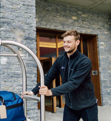 Smiling VIP staff member moving luggage on trolley outside Bear Lodge in Les Arcs