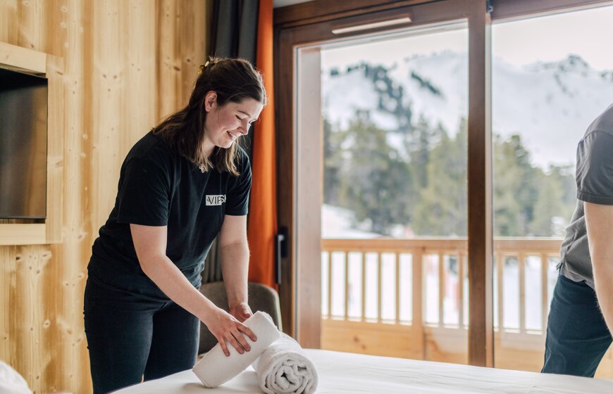 Woman wearing black VIP SKI polo shirt laying fresh towels on a bed in ski hotel