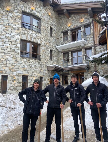 Four smiling VIP SKI staff members holding snow clearing shovels