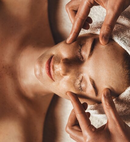 Woman with hair wrapped in towel having relaxing face massage