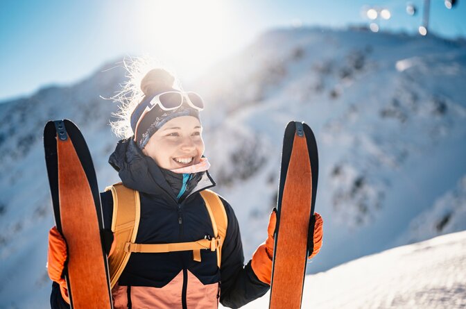 Smiling woman standing at top of snowy mountain holding up ski touring skis