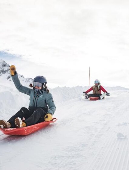 Two women sleding down hill with arms in the air