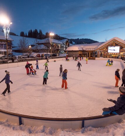 Families ice skating on floodlight open-air ice rink in Les Gets village