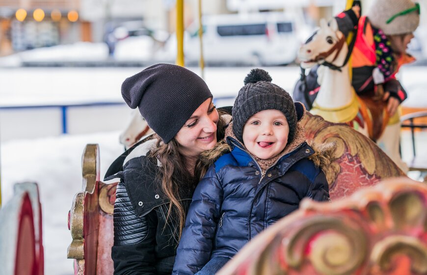 Smiling child sitting on mother's lap on traditional carousel in Les Gets