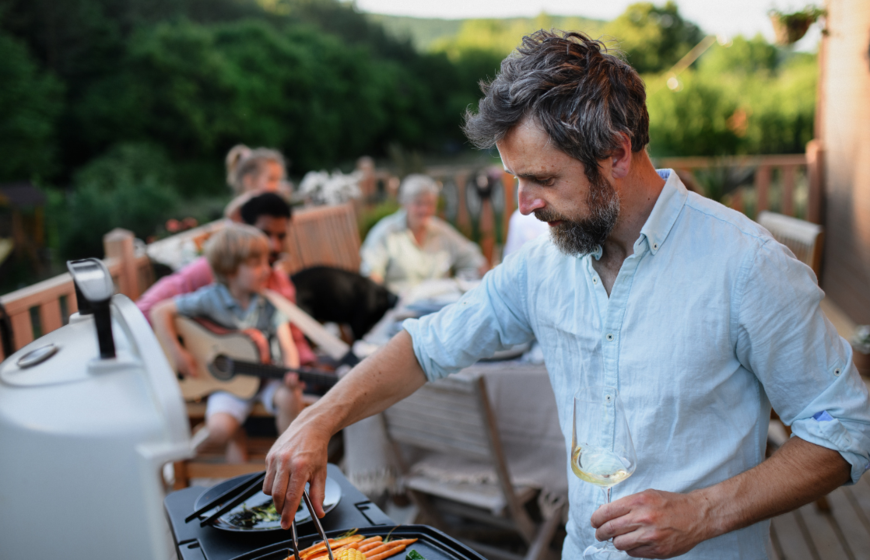 Man holding glass of wine cooking food on BBQ