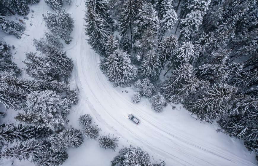 Aerial view of silver car driving along snowy road