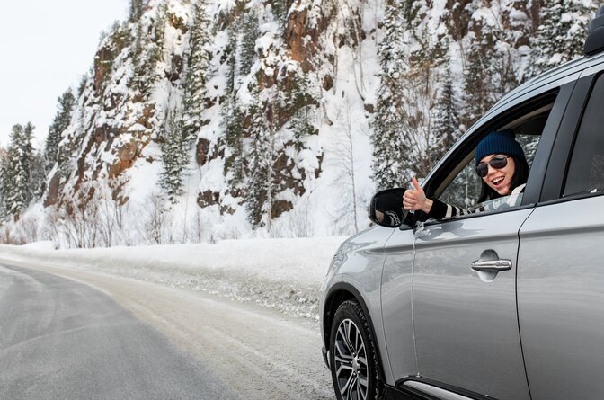 Smiling woman giving thumbs up from grey car on snowy mountain road