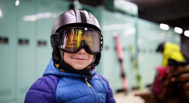 Smiling young boy wearing ski helmet and goggles in ski locker room