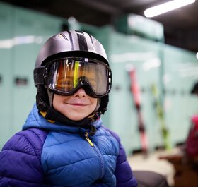 Smiling young boy wearing ski helmet and goggles in ski locker room