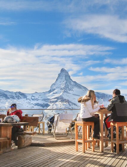 Skiers enjoying drinks at outdoor mountain bar in Zermatt with views of the Matterhorn in the background