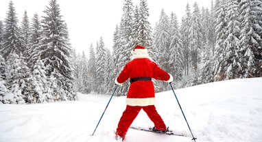 Rear view of Santa skiing snowplough down a snowy piste