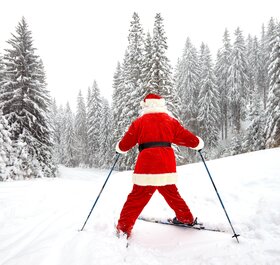 Rear view of Santa skiing snowplough down a snowy piste