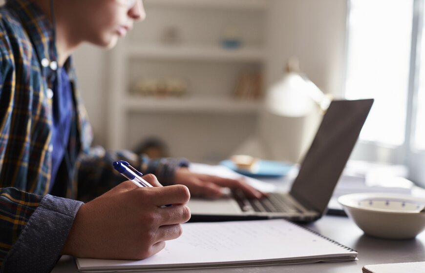 Boy with notepad working at laptop