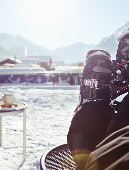 Skier resting ski boots on coffee table on terrace by ski slopes