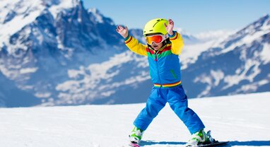 Young boy skier snowploughing with hands in air