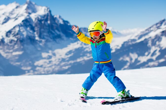 Young boy skier snowploughing with hands in air