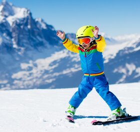 Young boy skier snowploughing with hands in air