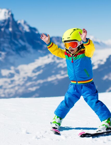 Young boy skier snowploughing with hands in air