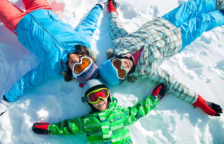 Mother and two children in ski gear lying down on snow looking up at camera