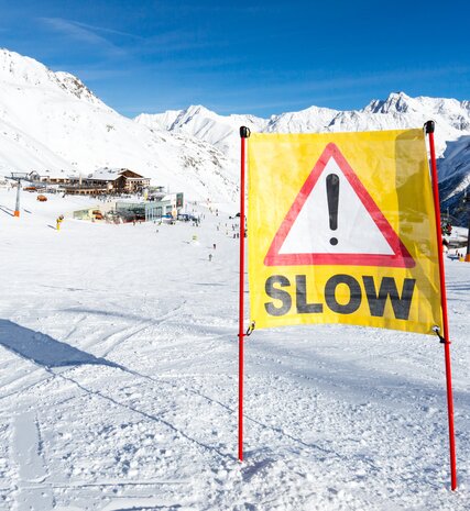 Slow sign in middle of ski slope coming down towards ski lift and mountain restaurants