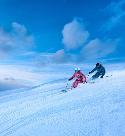 Two skiers skiing carved turns on groomed piste in La Plagne