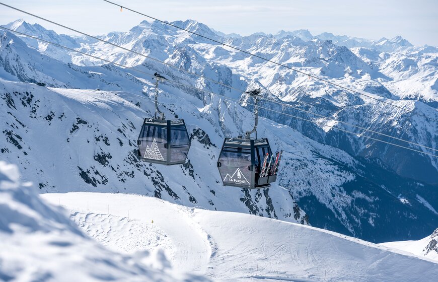 Two black gondolas in La Plagne about to pass each other with snowy mountains in the background