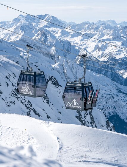 Two black gondolas in La Plagne about to pass each other with snowy mountains in the background