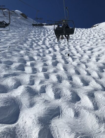 Lone skier tackling deep mogul field below chairlift