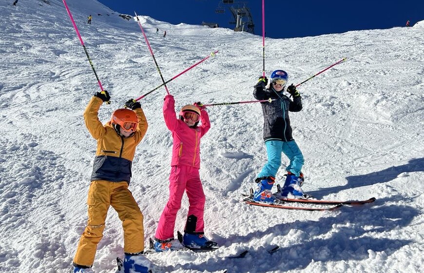 Three smiling young skiers with poles in the air at side of the Swiss Wall piste