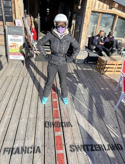 Female skier straddling border markings between France and Switzerland on mountain restaurant terrace