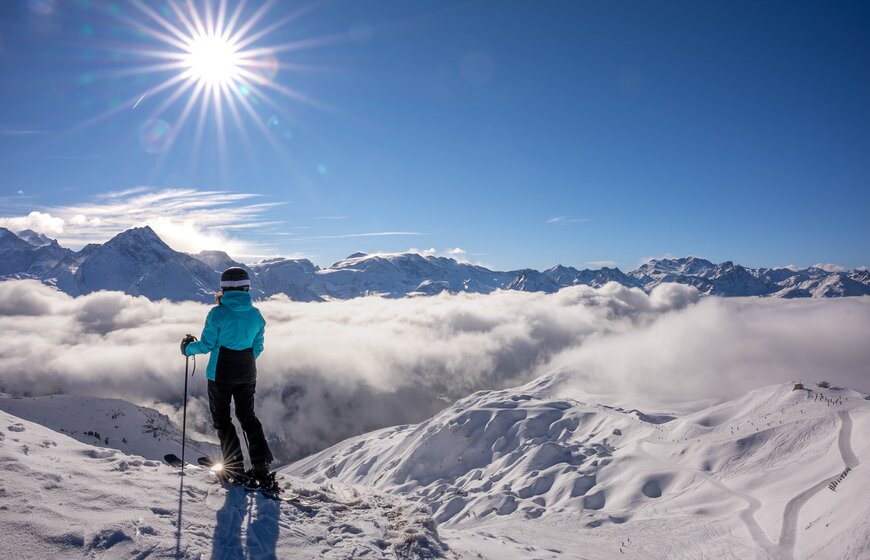 Female skier enjoying view of cloud inversion from top of snowy mountain in La Plagne