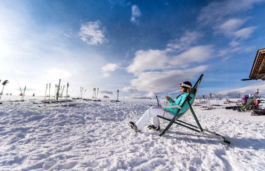 Female skier looking at mobile phone from deckchair outside mountain restaurant