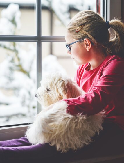 Girl sat in a window with a small dog on her lap