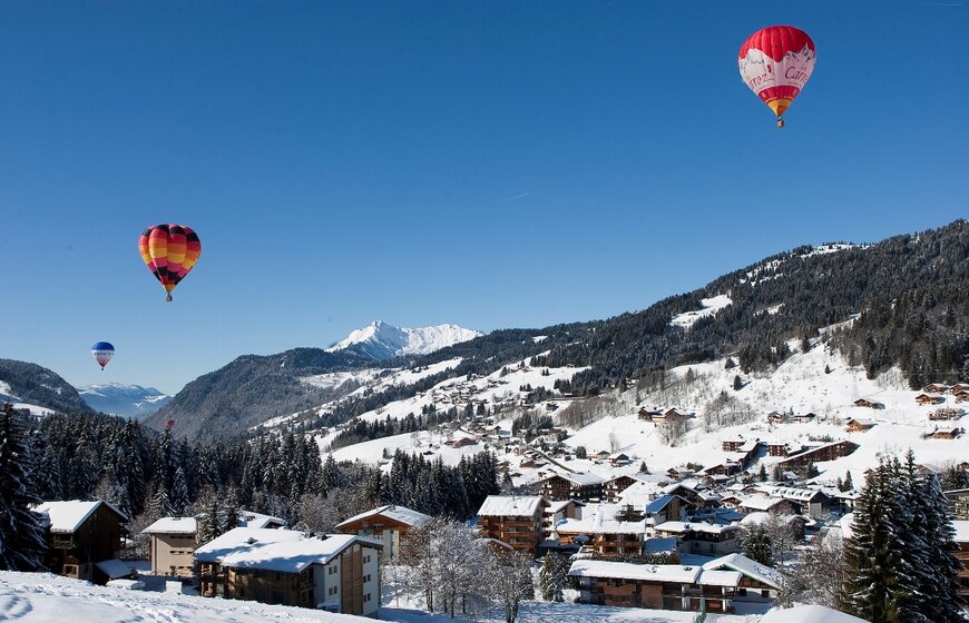 3 hot air balloons flying up above a snowy Les Gets