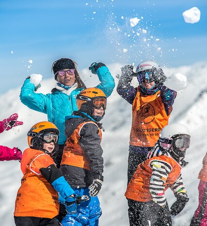 Children in ski school throwing snowballs with female ski instructor on sunny day