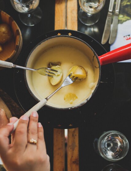 Two people dipping boiled potatoes into cheese fondue